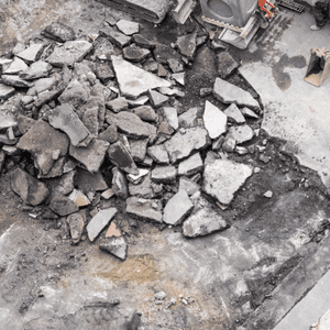 A large pile of concrete removal debris shows broken slabs scattered across a construction site