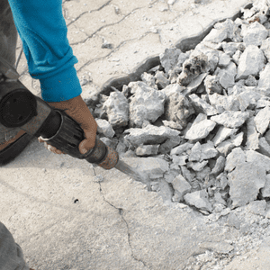 A construction worker uses a jackhammer for efficient concrete removal on a cracked driveway