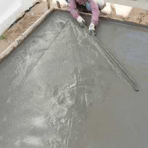 A worker uses a screed tool for concrete restoration and surface leveling of a slab