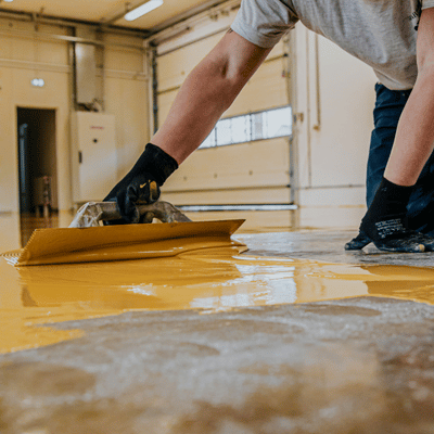Technician spreads vibrant yellow epoxy resin onto floor surface, highlighting durability in polished concrete vs epoxy