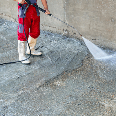 Worker uses pressure washer before applying overlay, demonstrating what is resurfacing concrete preparation