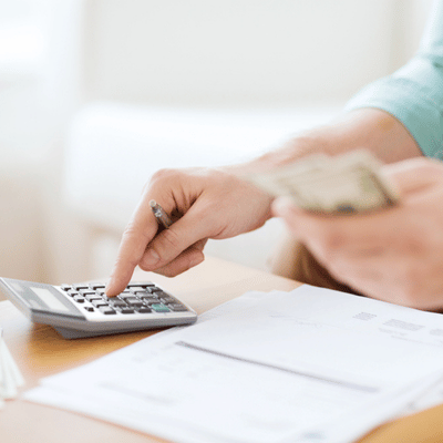 Homeowner calculates project expenses with calculator and cash while reviewing estimates and invoices on table