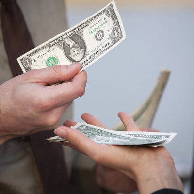 Close-up of two people exchanging US dollar bills during a payment transaction in natural lighting