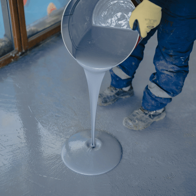 Contractor pours self-leveling gray compound after concrete floor stripping, creating smooth surface for finishing work
