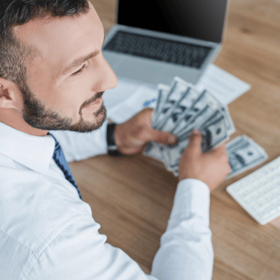 Businessman counts cash at desk near laptop, evaluating expenses and savings for flooring renovation estimates