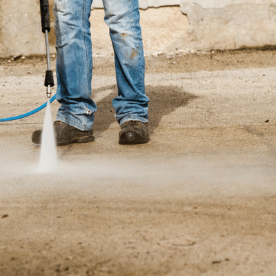 Worker pressure-washes driveway pavers, demonstrating how to care for concrete floors and remove grime effectively