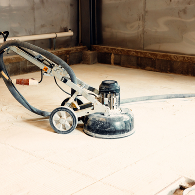 Floor grinder sits on dusty slab, illustrating grind and seal vs polished concrete process comparison