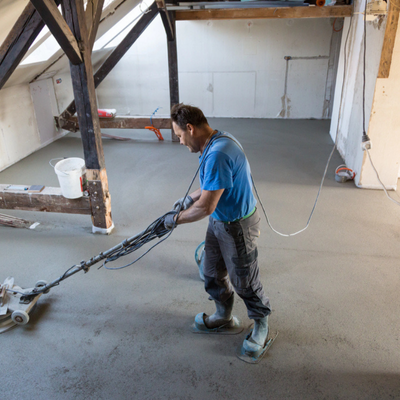 Contractor power-trowels newly poured concrete floor, smoothing surface evenly during interior renovation project this week