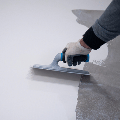 Installer smooths grey coating with notched trowel, discussing best epoxy color for garage floor choices