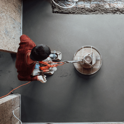 Overhead view of worker guiding power trowel along edges, refining slab to uniform sheen finish