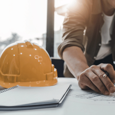 Worker reviews plans beside hard hat and notebook, coordinating concrete staining services for project planning