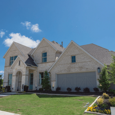 New stone home exterior under blue sky, showcasing driveway potential for concrete staining services outdoors