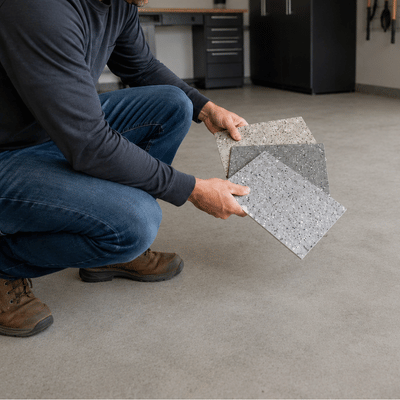 A contractor reviews garage floor coating fort worth samples while kneeling on a plain concrete garage floor