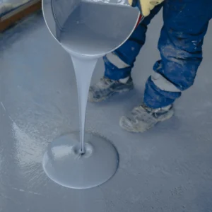 A worker pours gray epoxy coating onto a concrete floor during installation